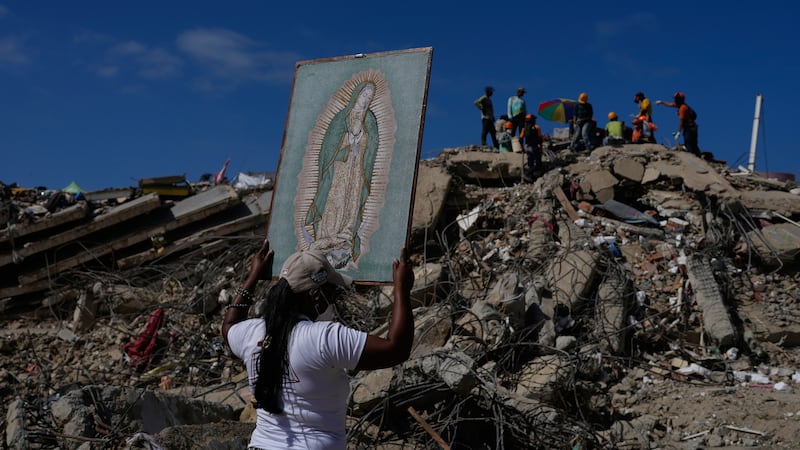 A woman holds a painting of the Virgin Mary as she accompanies a Catholic priest supporting...